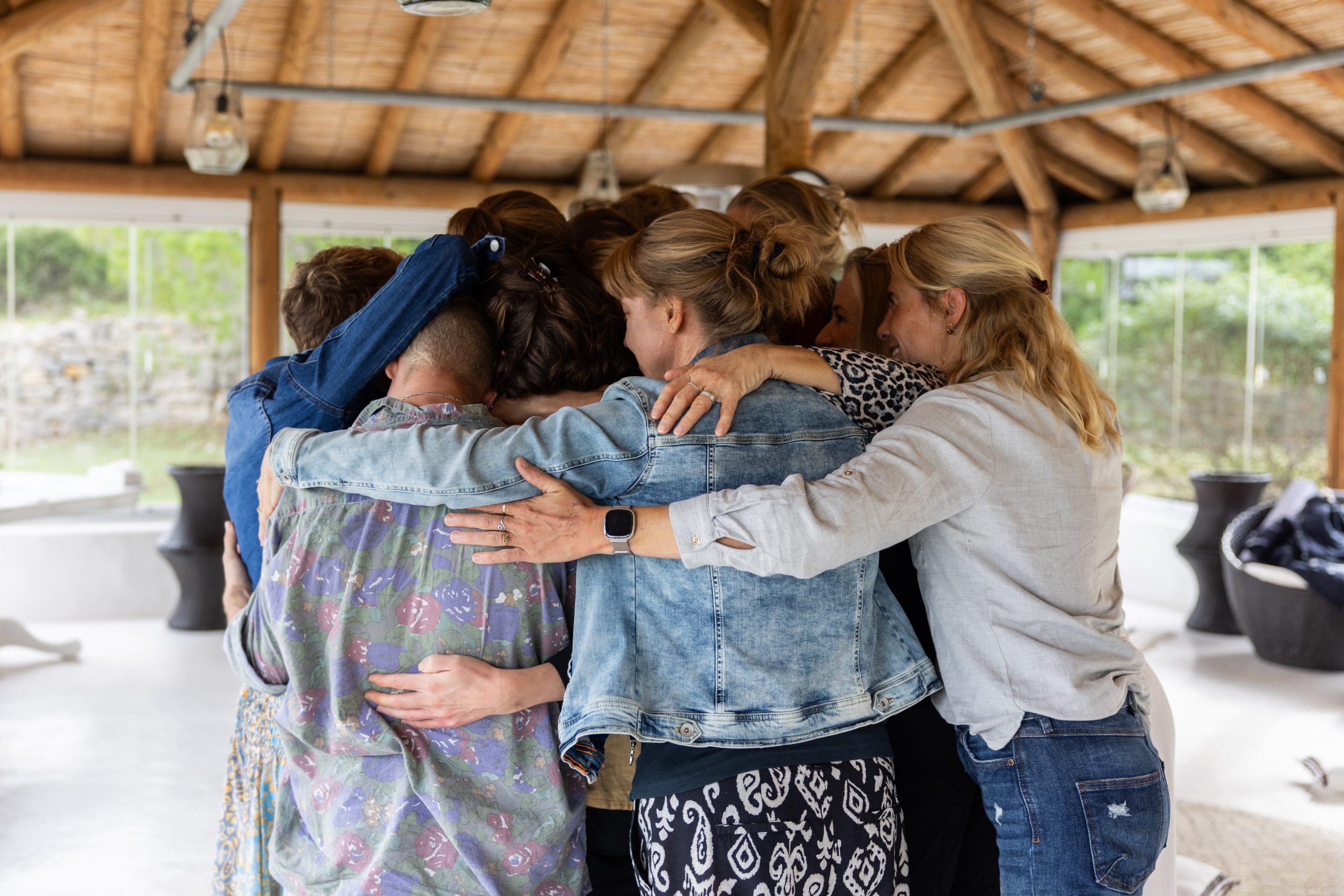 Groep volwassenen in groepsomhelzing tijdens ondersteunende sessie in rieten paviljoen, sfeer passend bij ambulante of residentiële eetstoornis behandeling van BeLeef.